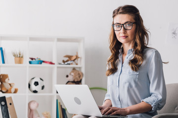child psychologist sitting in armchair with laptop and looking at camera