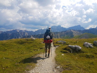 Hiker with backpack walking a trail on top of a mountain and enjoying valley view during trip in the alps