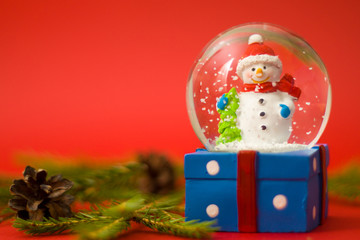 Christmas and new year card with snow globe snowman inside. Gift box on red background. Holidays, winter and celebration concept.