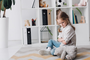 depressed little child sitting on floor with teddy bear