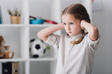 close-up portrait of sad little child covering ears with hands and looking away - obrazy, fototapety, plakaty