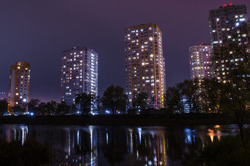 Fototapeta na wymiar Apartment buildings with glowing windows near the pond at night.