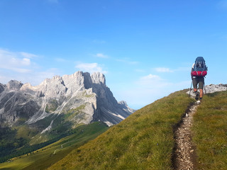 Hiker with backpack walking a trail on top of a mountain and enjoying valley view during trip in the alps