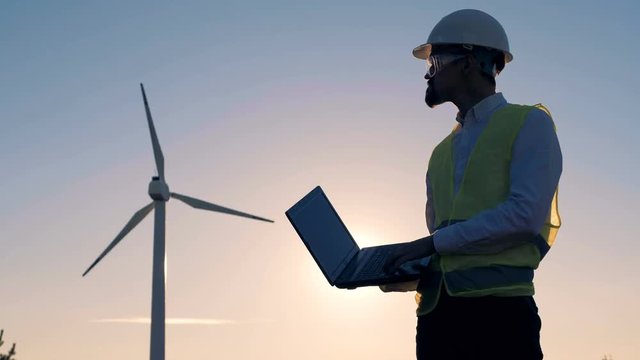 The sun is setting while an energetics expert is observing a windmill. Clean, eco-friendly energy concept.