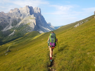 Hiker with backpack walking a grass trail on top of a mountain and enjoying valley view during trip in the alps