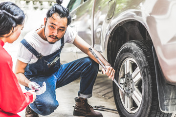 Naklejka premium Fixing car engine in automobile repair garage. Handsome mechanics in uniform are repairing car while working in auto service