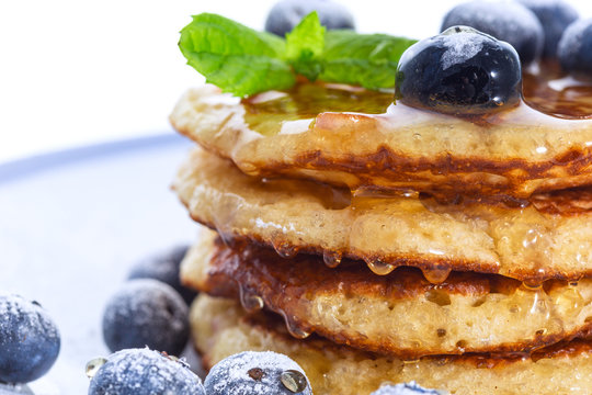 Pile of pancakes with blueberries sprinkled with icing sugar and poured on with honey