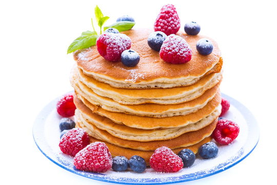 Pile of pancakes with blueberries and raspberries sprinkled with icing sugar
