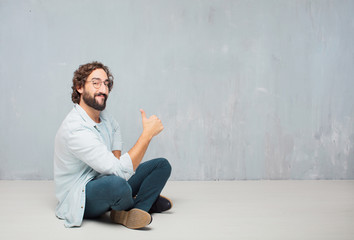 young cool bearded man sitting on the floor. grunge wall background