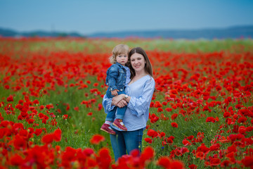 Obraz na płótnie Canvas beautiful young woman with child girl in poppy field. happy family having fun in nature. outdoor portrait in poppies. mother with daughter. summer time
