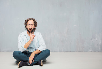 young cool bearded man sitting on the floor. grunge wall background