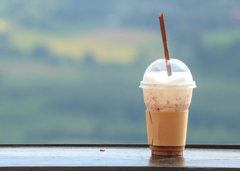 an iced coffee in plastic cup with natual view as background.