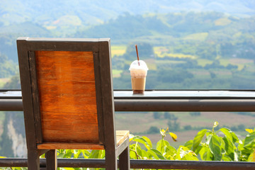 a back of wood seating chair and iced coffee cup with natural green view.