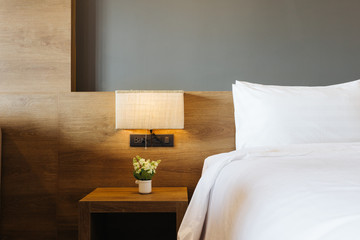 Close-up of white pillow on bed decoration with light lamp in hotel bedroom interior.