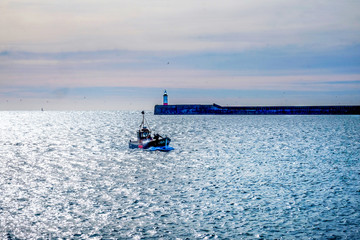 fishing boat entering Newhaven harbour with the lighthouse on the Quay behing in a glistening sea
