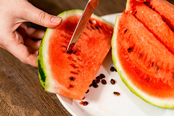 Sliced watermelon in a plate on a wooden table. A knife removes seeds from a lobule.