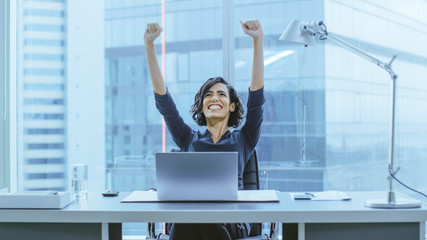 Shot of the Beautiful Businesswoman Sitting at Her Office Desk, Raising Her Arms in a Celebration...
