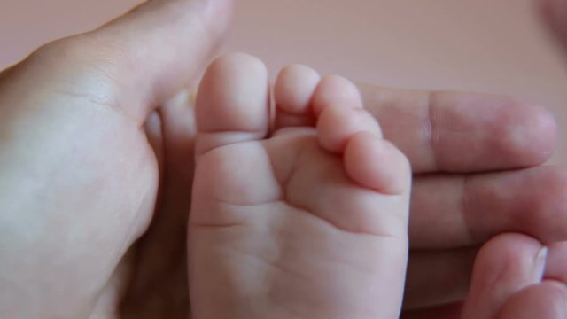 Close-up of child's legs in background with mother. Close-up of Little baby feet with mother hand. Children's legs in the hands of the mother. Tiny legs of a newborn baby on female hands close-up.