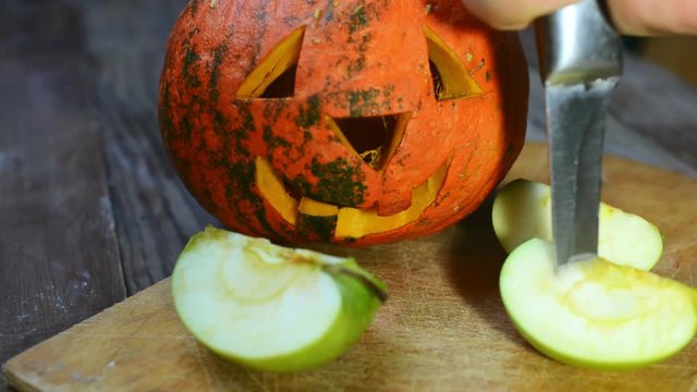 Knife punches an apple next to a pumpkin for Halloween