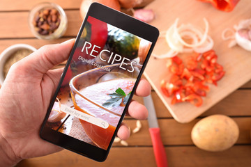 Using digital cookbook app in smartphone for cooking closeup - obrazy, fototapety, plakaty