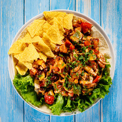 Grilled chicken meat with nachos and vegetables on wooden background