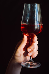 hand holds a glass of fresh red wine on a dark background