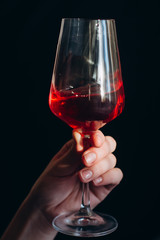 hand holds a glass of fresh red wine on a dark background