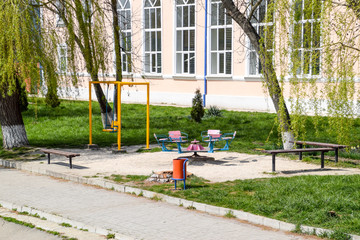 Fototapeta premium Mini playground under willow trees. Swing and carousel next to the benches