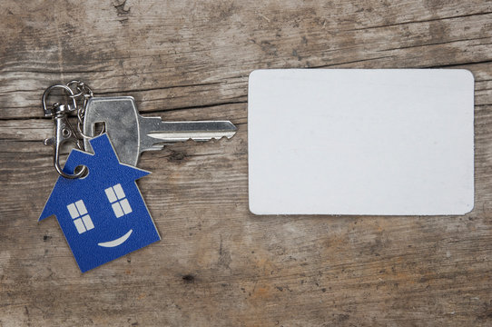 Key with house icon and white blank paper on wooden background