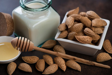 Bowl with unpeeled almonds, bottle of almond milk and honey with a wooden spoon, closeup, selective focus