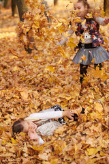 Child girl is lying and playing in fallen leaves in autumn city park.