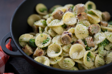 Close-up of a stewpan with italian orecchiette with broccoli sauce, pork sausages and parmesan, selective focus