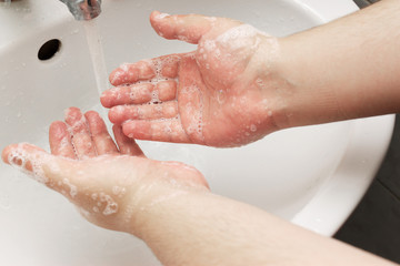 A man washes his hands with soap in the sink.