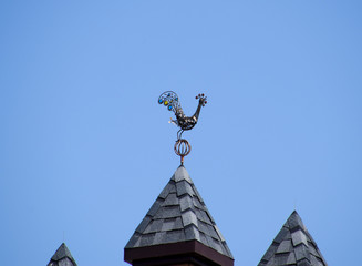 Fototapeta na wymiar Metal weather vane on top of the building. Weathervane in the form of a singing rooster.