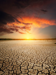 red sunset in dramatic clouds over drought earth