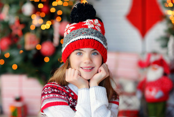 portrait of a beautiful 9-year-old girl in a knitted red hat in a New Year's interior