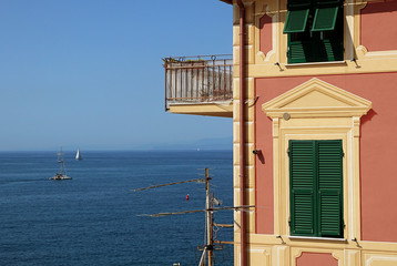 Fototapeta na wymiar Genoa, - View of blue Tigullio gulf from the rocky cape closing Boccadasse bay and the profile of a characheristic Ligurian painted house