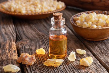 A bottle of frankincense essential oil with frankincense resin on a rustic background - obrazy, fototapety, plakaty