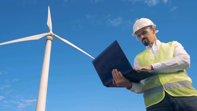 Inspector in warnvest is observing a functioning windmill with his laptop