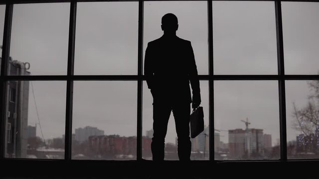 businessman stands at the window in the office and looks at the city. 4K