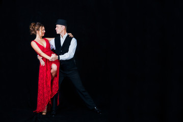 Young beautiful woman in red dress and guy dancing tango on black background in Studio