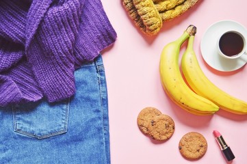 Feminine lifestyle photo. Flat lay woolen sweater, jeans, yellow hat and bunch of bananas, oatmeal cookies, cup of coffee and pink lipstick