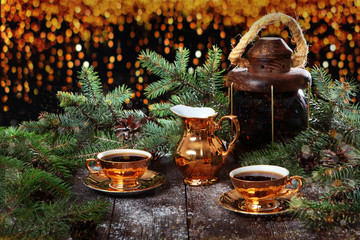 Two cups of coffee with gold color and milkman on the background of fir branches. Wooden background and garlands. New year holidays and Valentine's day.