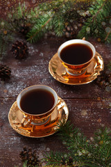 Two cups of coffee with gold color on a wooden background and on the background of fir branches. New year holidays and Valentine's day. Breakfast for two.