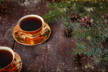 Two cups of gold color with coffee on a wooden background and with fir branches. Concept holidays New year and Valentine's day, Christmas.