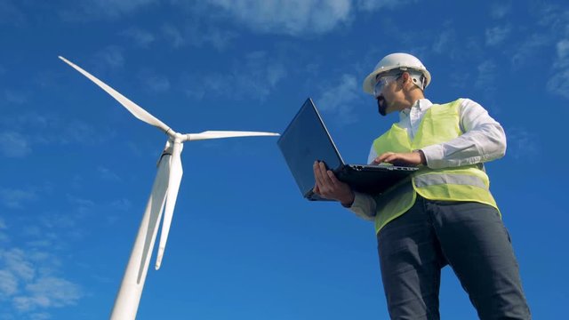 Blue sky with a turbine tower getting controlled by an engineer with a laptop