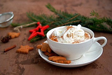 Hot cocoa in a white cup in a New Year's decoration on a brown background. Served with ginger biscuits and whipped cream.
