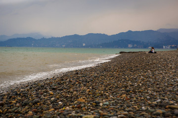 Fototapeta na wymiar Empty pebble beach of Batumi in cloudy weather. A lonely couple of people on the beach in a storm