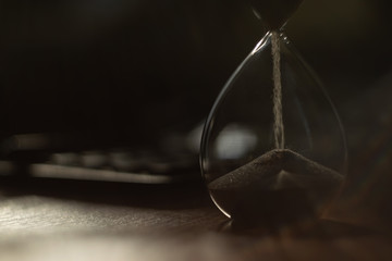 The hourglass is on the table. In the background there is a calculator. The flow of sand is...