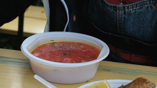 Tourist eats borscht from plastic dishes in an outdoor cafe. Close up.